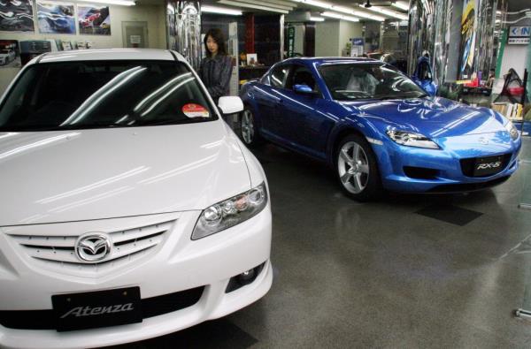 A customer looks at a Mazda Atenza sedan next to an RX-8 sports car 