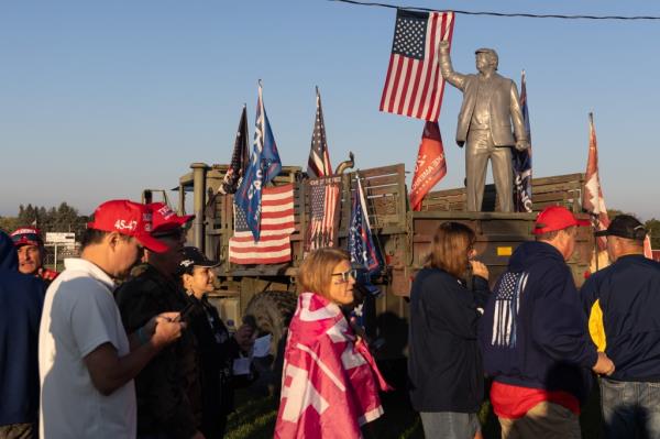 People walk past a statue of Trump during early in the morning while waiting to get into the rally.  