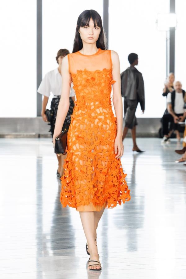 A woman in an orange dress walking down the runway at the SIMKHAI SS25 NYFW, photo by Bahram Hakkakian